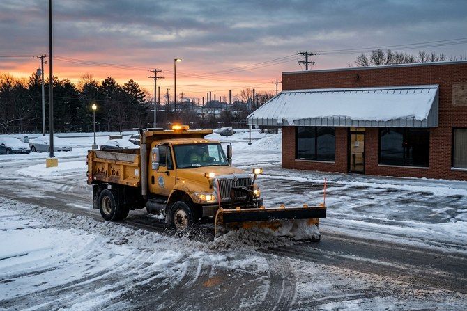Snow plow truck clearing a commercial parking lot at dawn